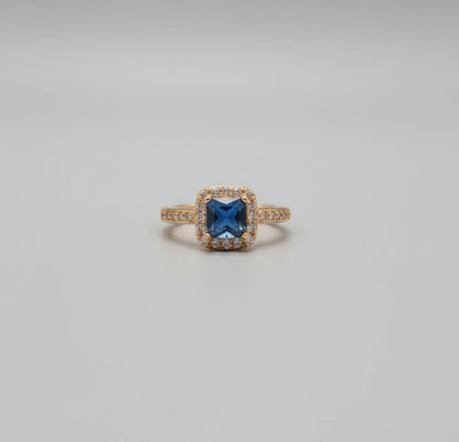 Gold ring with a blue gemstone on a reflective surface