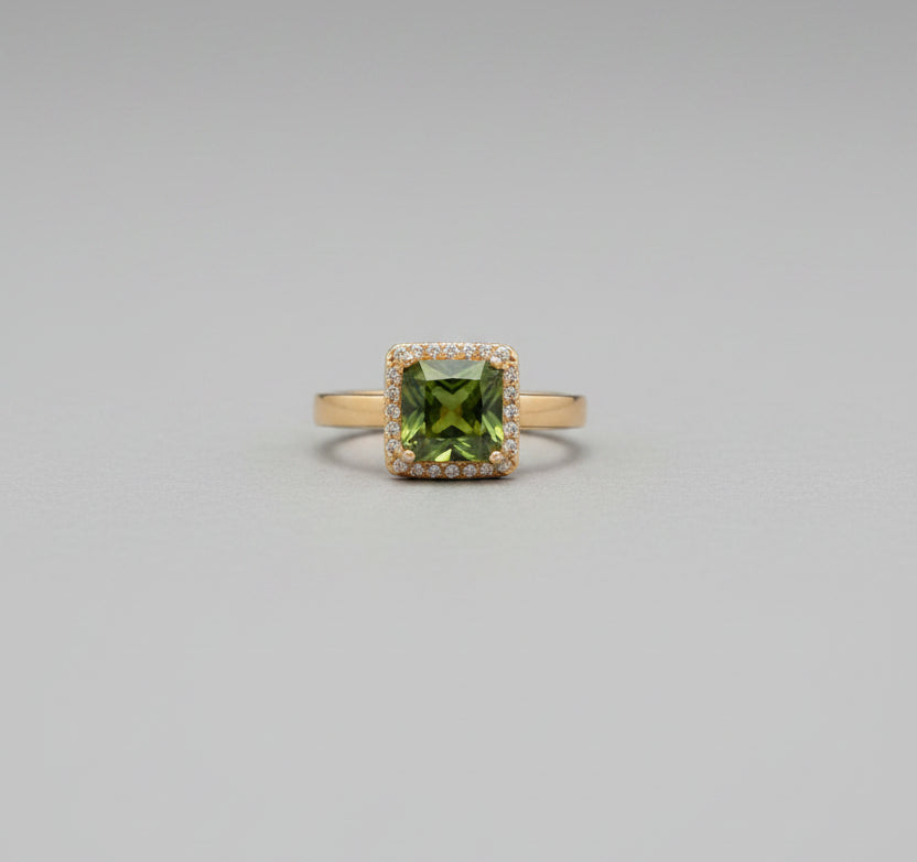 Ring with a green gemstone on a reflective surface, blurred background