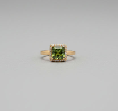 Ring with a green gemstone on a reflective surface, blurred background