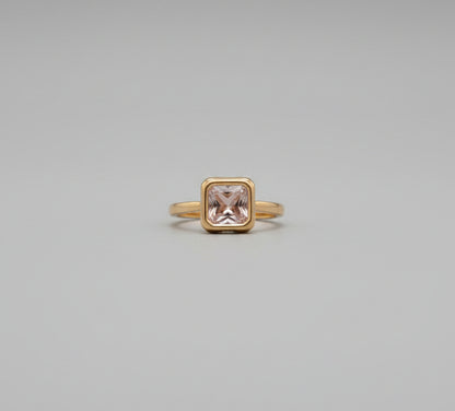 Gold ring with a pink gemstone on a reflective surface, blurred background