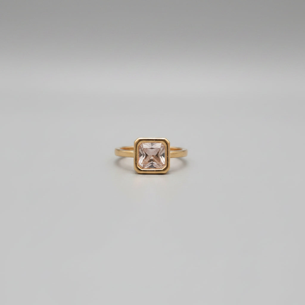 Gold ring with a pink gemstone on a reflective surface
