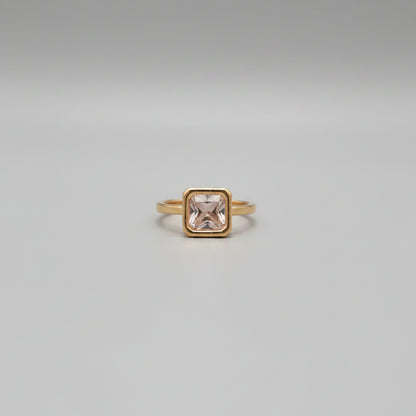 Gold ring with a pink gemstone on a reflective surface