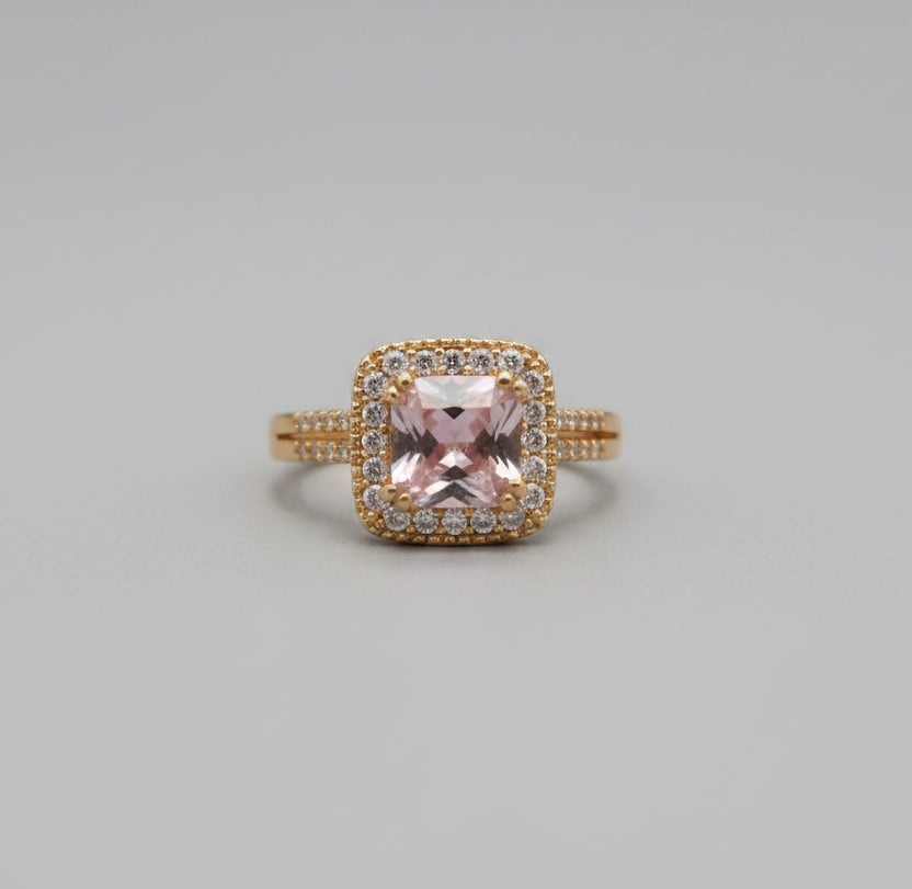 Gold ring with a pink gemstone on a reflective surface