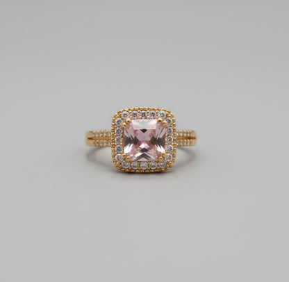 Gold ring with a pink gemstone on a reflective surface