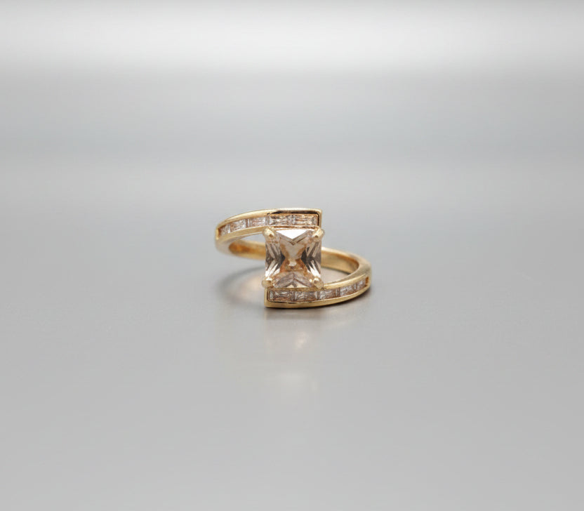 Gold ring with a square stone on a reflective surface