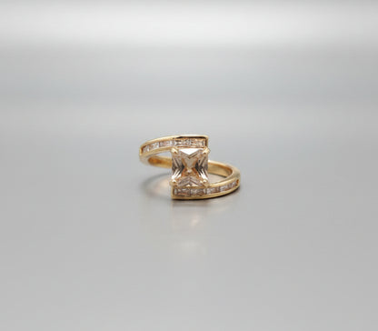 Gold ring with a square stone on a reflective surface