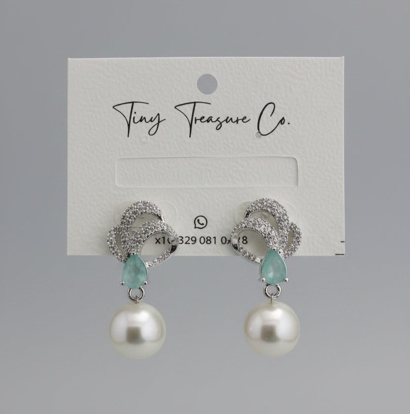 Pearl and turquoise earrings on a 'Tiny Treasure Co.' card held by a hand.