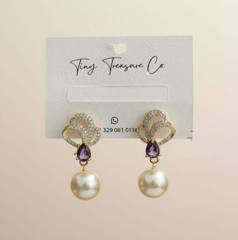 Pearl earrings with gold accents held by a hand on a gray surface.