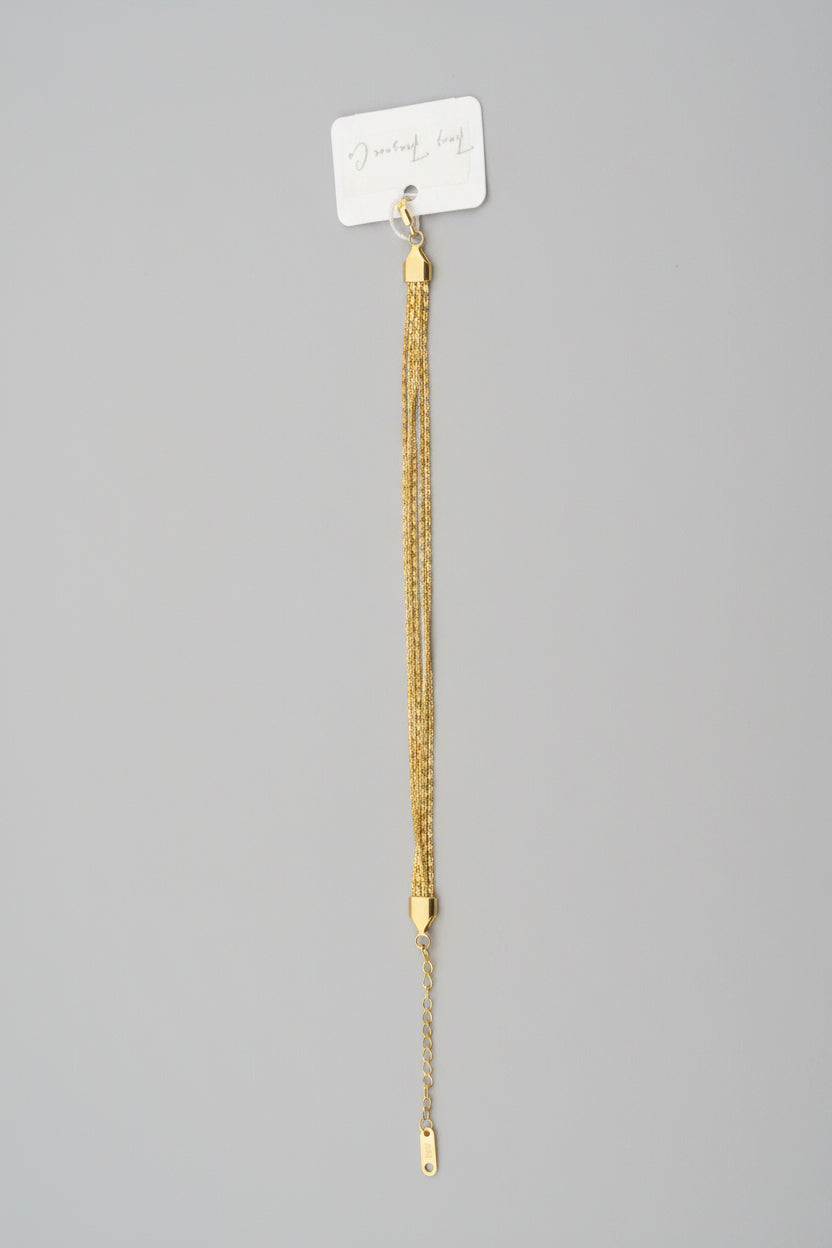 Gold bracelet on a gray surface with a white label