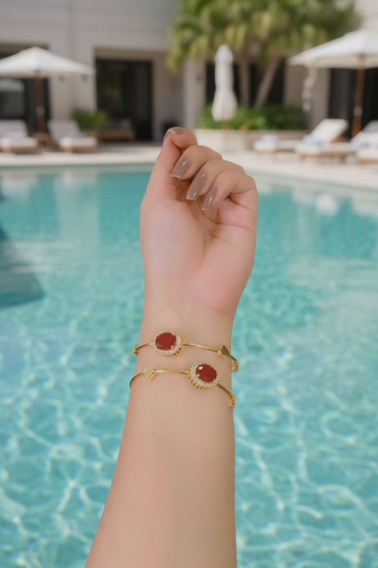 Hand wearing two gold bracelets with red stones on a dark background